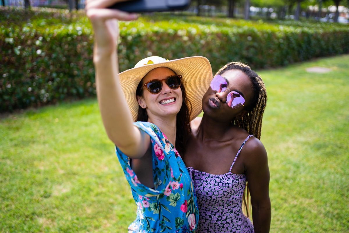 Two multiethnic friends with summer dresses taking a selfie outdoors